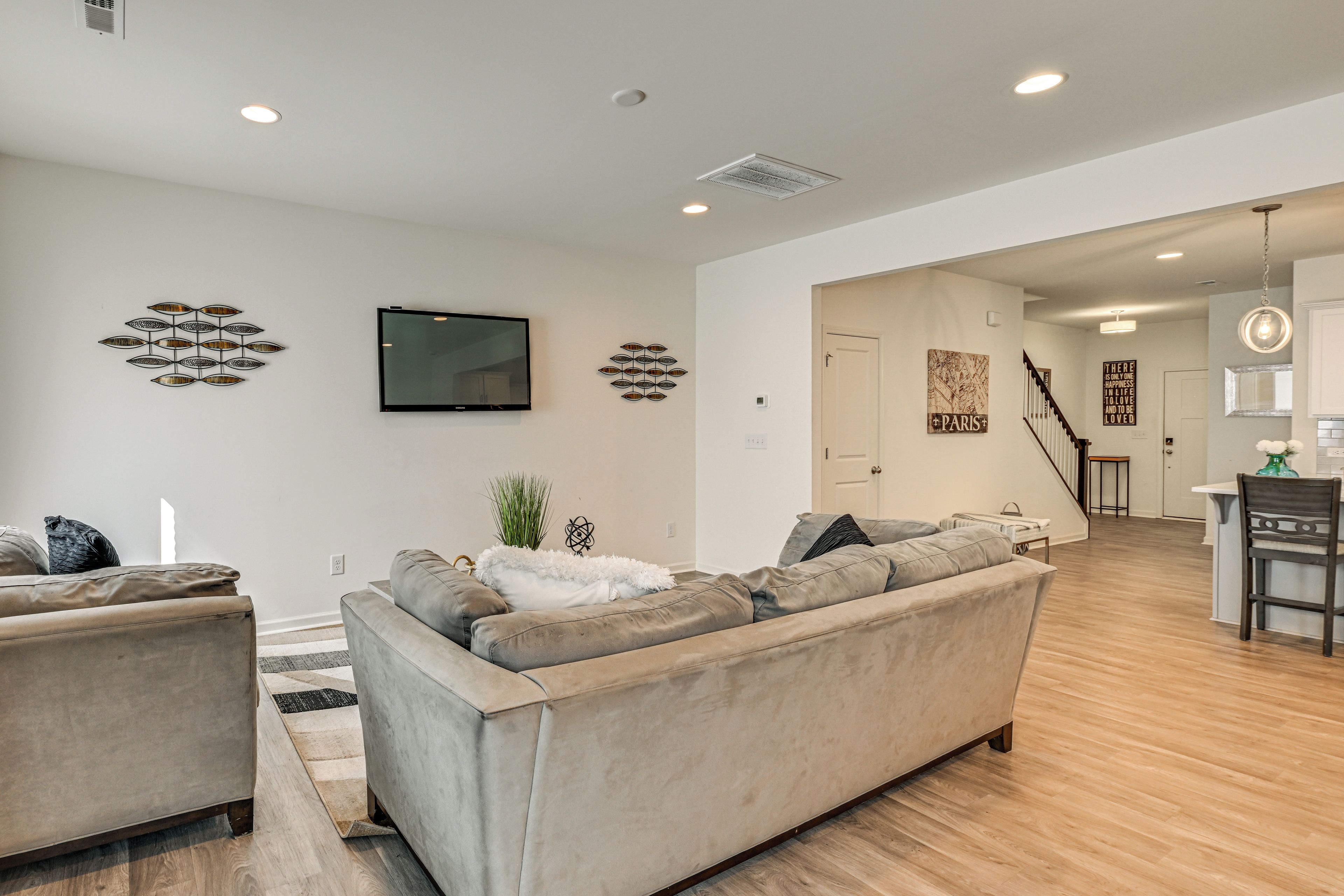 A modern living room with a sofa, a flat-screen TV, decorative wall art, and a staircase leading to another area.