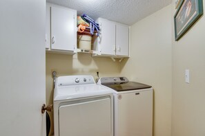 A compact laundry room with a washing machine and dryer, a drying rack above the dryer, and a small cabinet with various items. - Steps to Sand! Extended Bradenton Beach Getaway (Bradenton Beach)