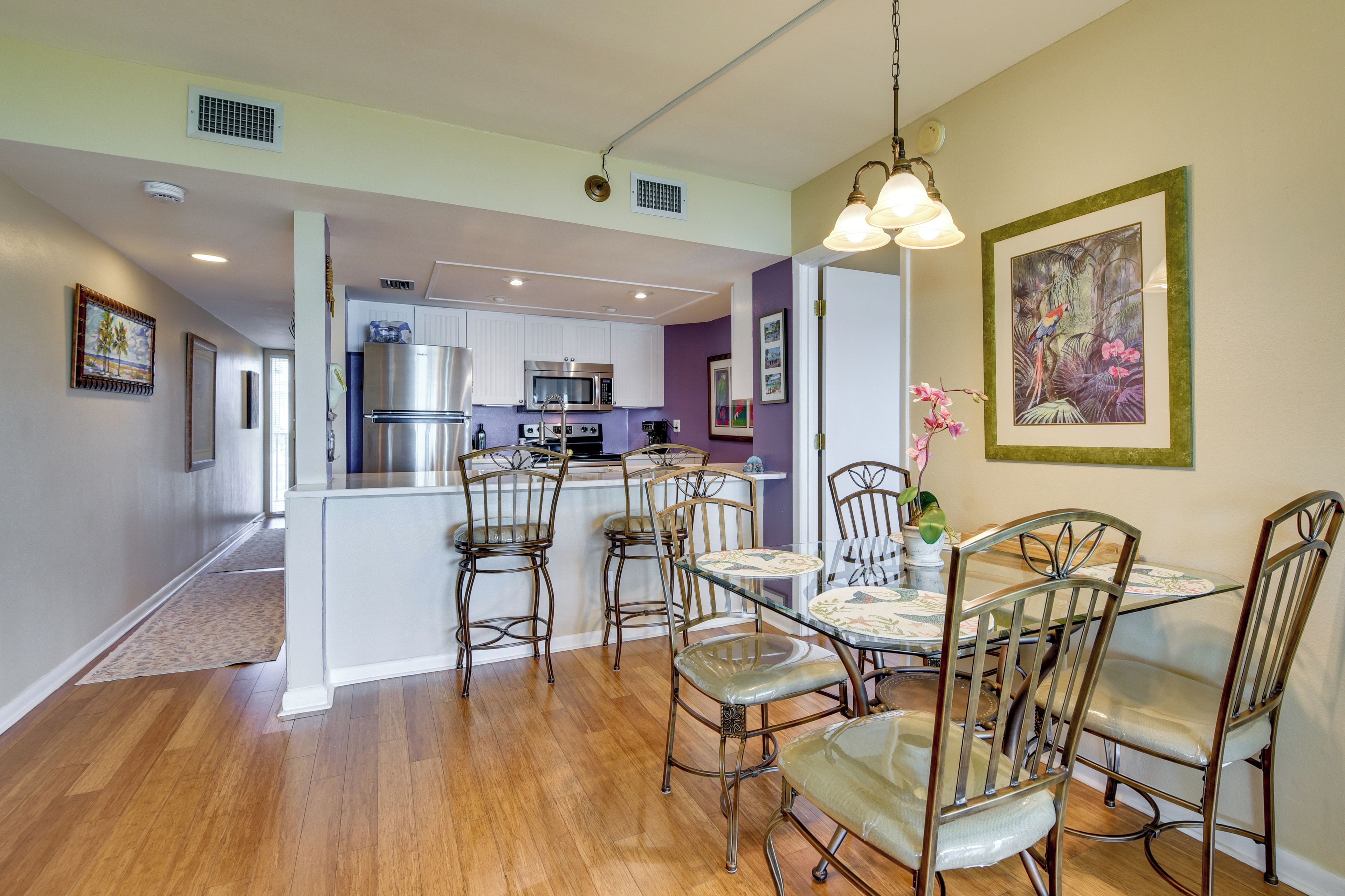 A modern kitchen with stainless steel appliances, a dining area with a glass table and metal chairs, and a hallway leading to another room.