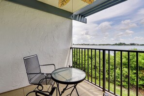 A balcony with a metal chair and table, overlooking a body of water and greenery. - Steps to Sand! Extended Bradenton Beach Getaway (Bradenton Beach)