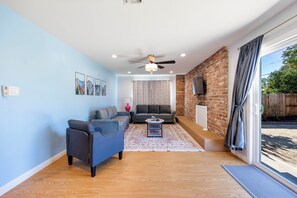 Sala de estar com parede azul, ventilador de teto, lareira e uma janela grande com cortinas.
