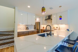 Una cocina moderna con armarios blancos, encimera de mármol, horno empotrado y refrigerador de acero inoxidable.