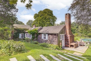 A rustic house with a chimney, a small porch, and a swimming pool.