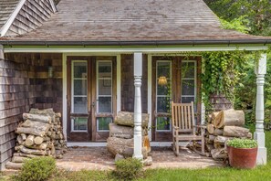 A wooden porch with a chair and logs, a brick pathway, and a white railing.