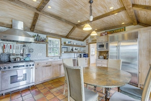 A kitchen with a wooden ceiling, stainless steel appliances, and a round dining table.