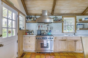 A kitchen with a stainless steel range, wooden cabinets, a tiled backsplash, and a window with a view of greenery.