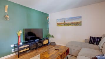 A living room with a flat-screen TV, a wooden coffee table, a grey sofa, and a painting of a desert landscape.