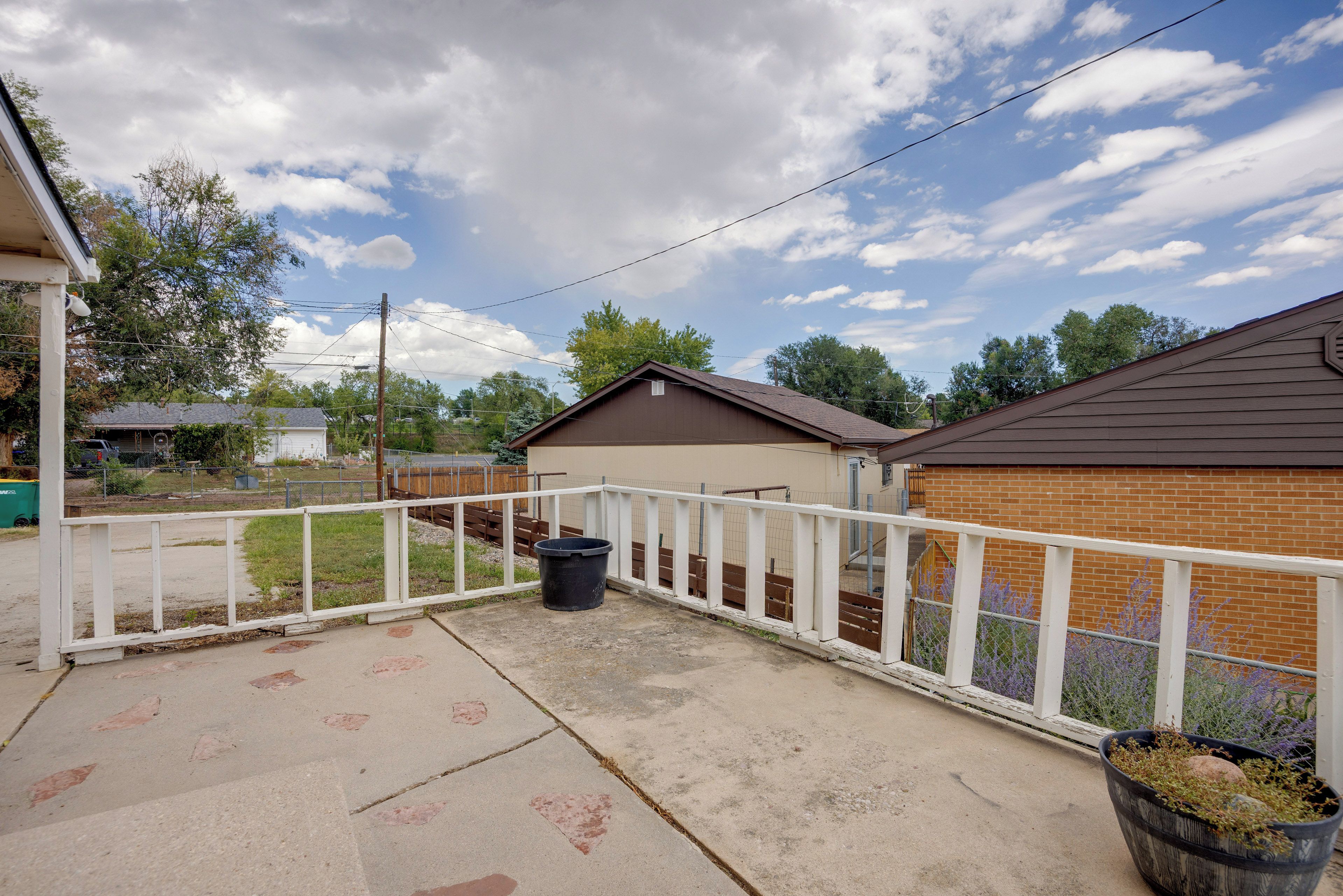 A residential backyard with a white fence, a trash bin, and a potted plant.