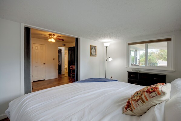 A bedroom with a bed, a window, a door, and a hallway.