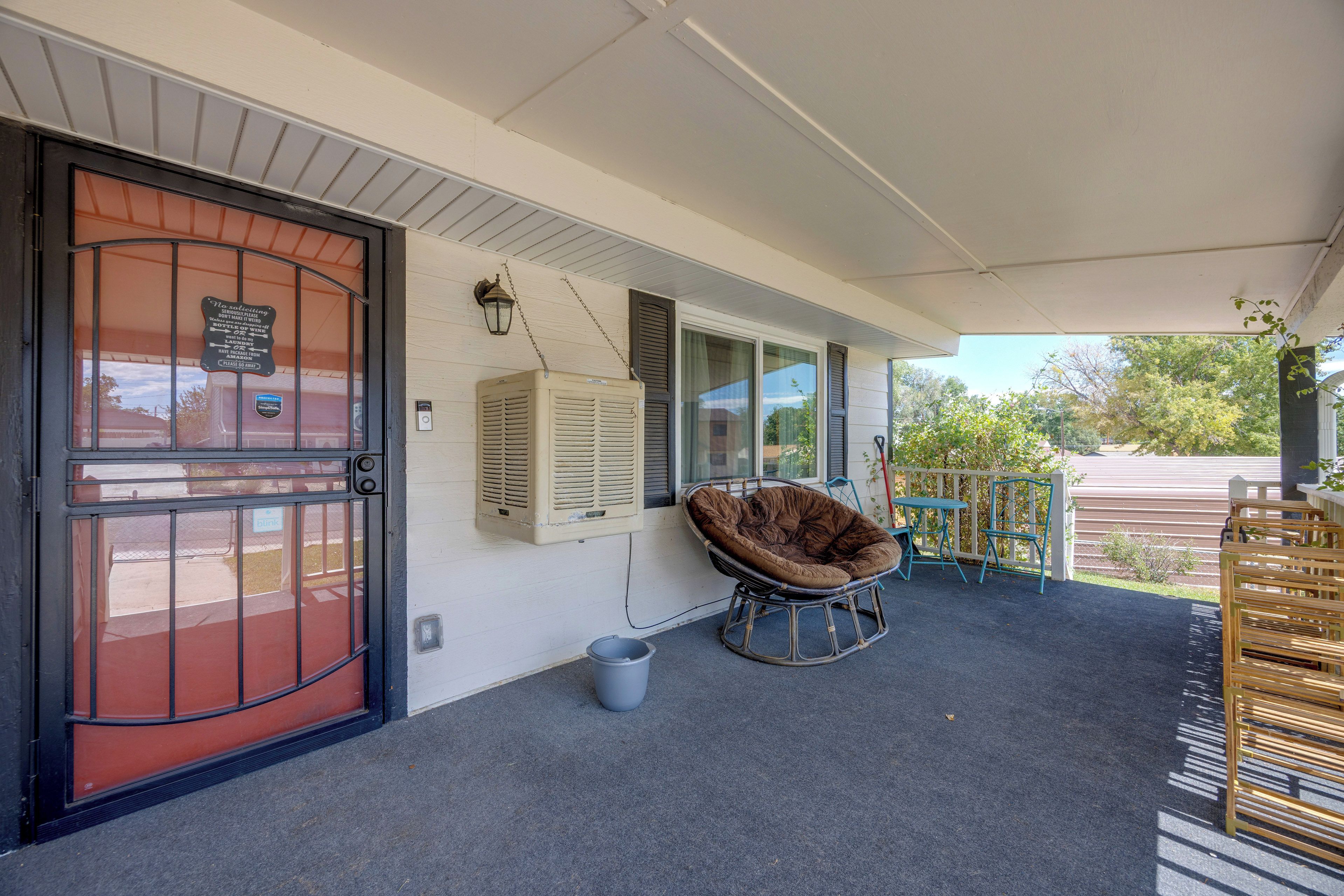A covered porch with a swing chair, a door with a sign, and a window with shutters.