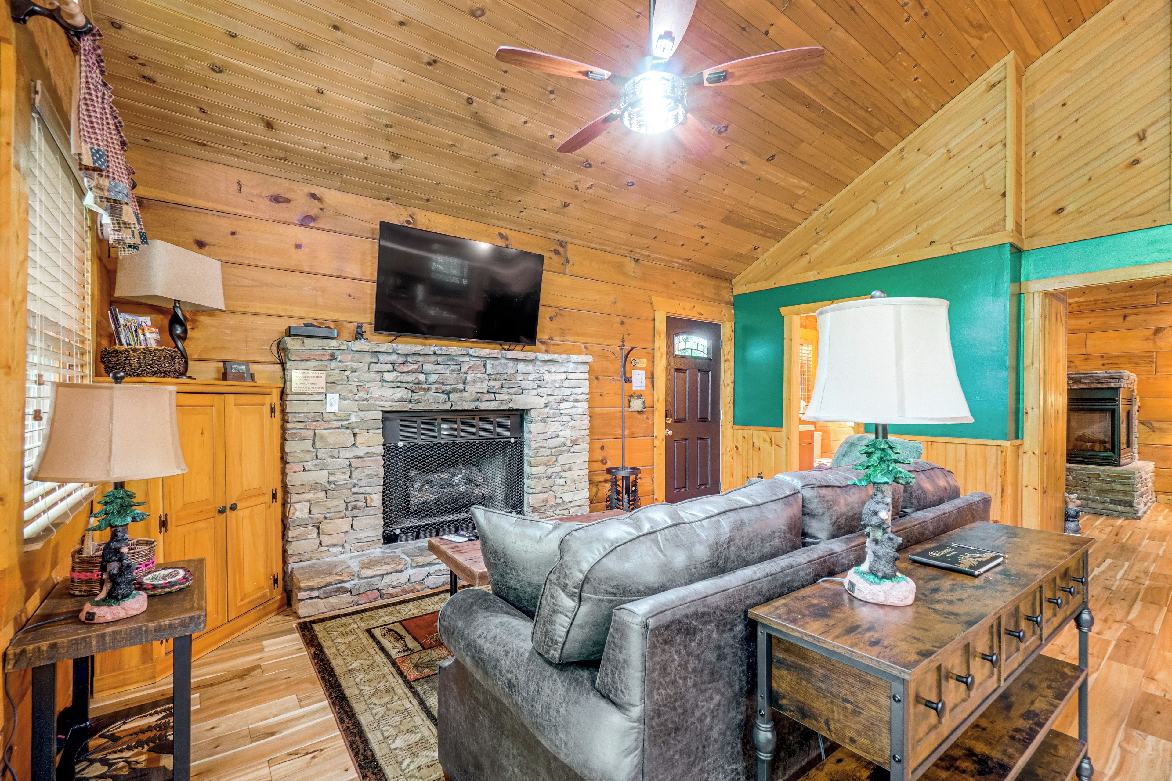 Interior acogedor de una cabaña de madera con chimenea de piedra, sofá de cuero y televisor de pantalla plana montado encima.