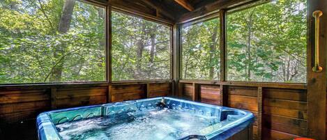 Una cabaña de madera con jacuzzi y grandes ventanales con vistas a un bosque.