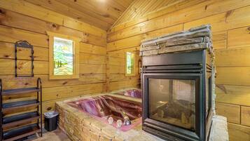 A cozy cabin interior with a stone fireplace, wooden walls, and a window with a view of trees.