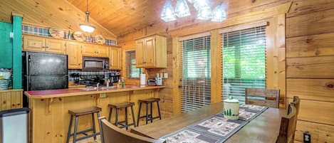 Interior de una cabaña de madera con cocina, comedor y asientos de bar.