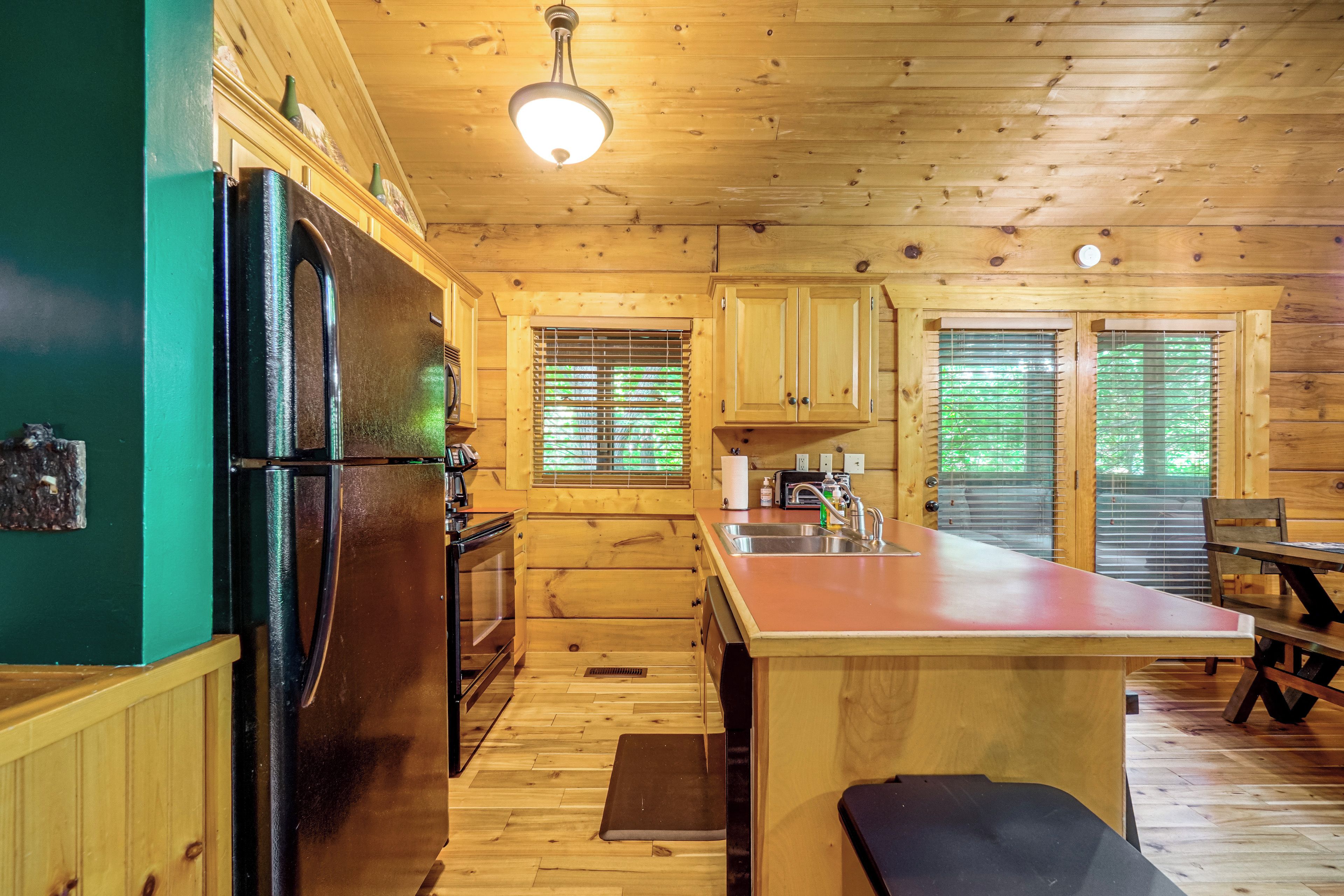A wooden cabin interior with a kitchen area, including a refrigerator, stove, and wooden cabinets.