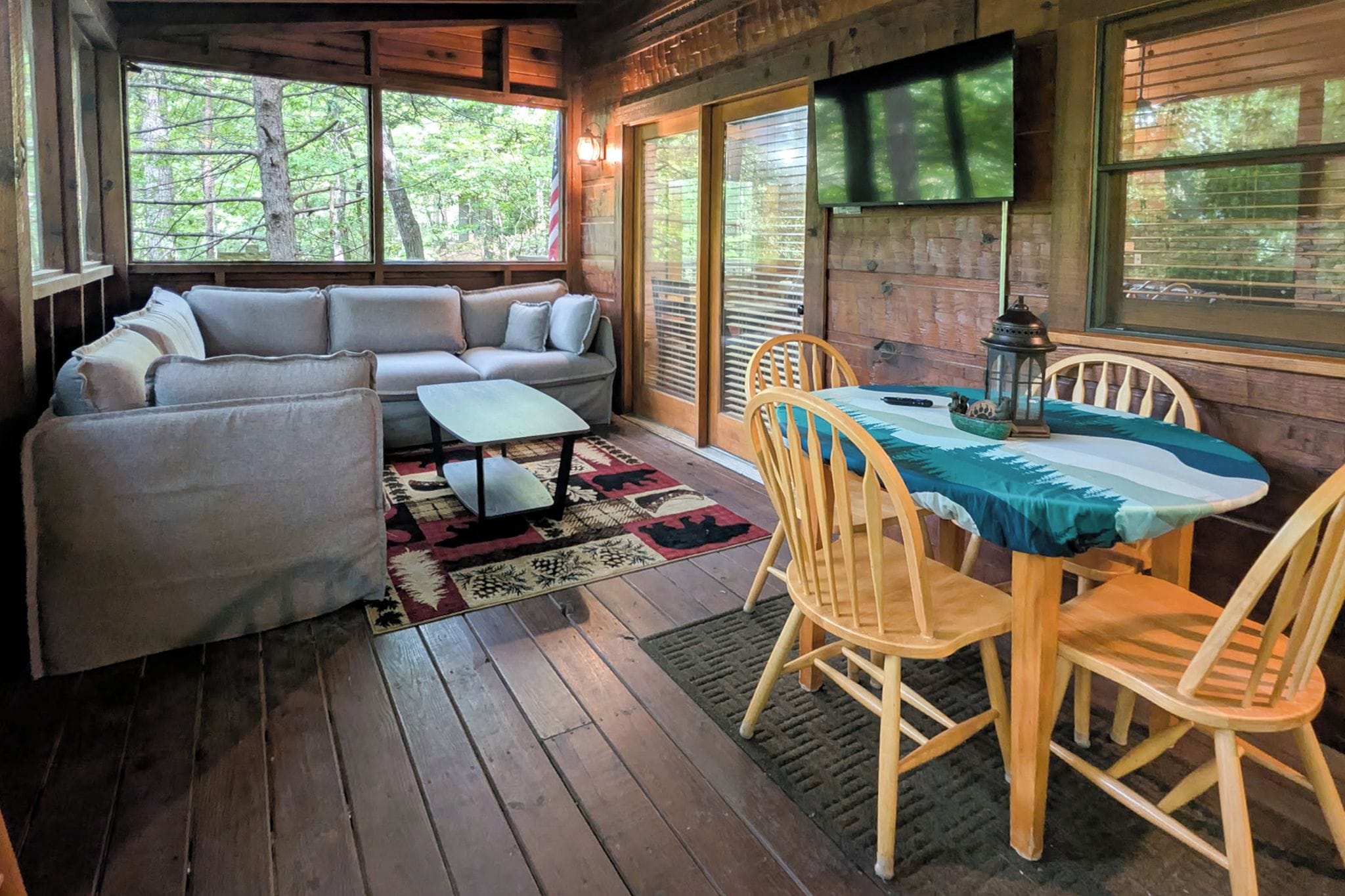 A cozy cabin interior with a sofa, a dining table with chairs, and a TV mounted on the wall.