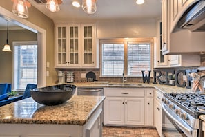 A kitchen with granite countertops, white cabinetry, a large island with a bowl, a coffee maker, and a stove. - Walk to Texas Tech! Upscale Family Retreat (Lubbock)