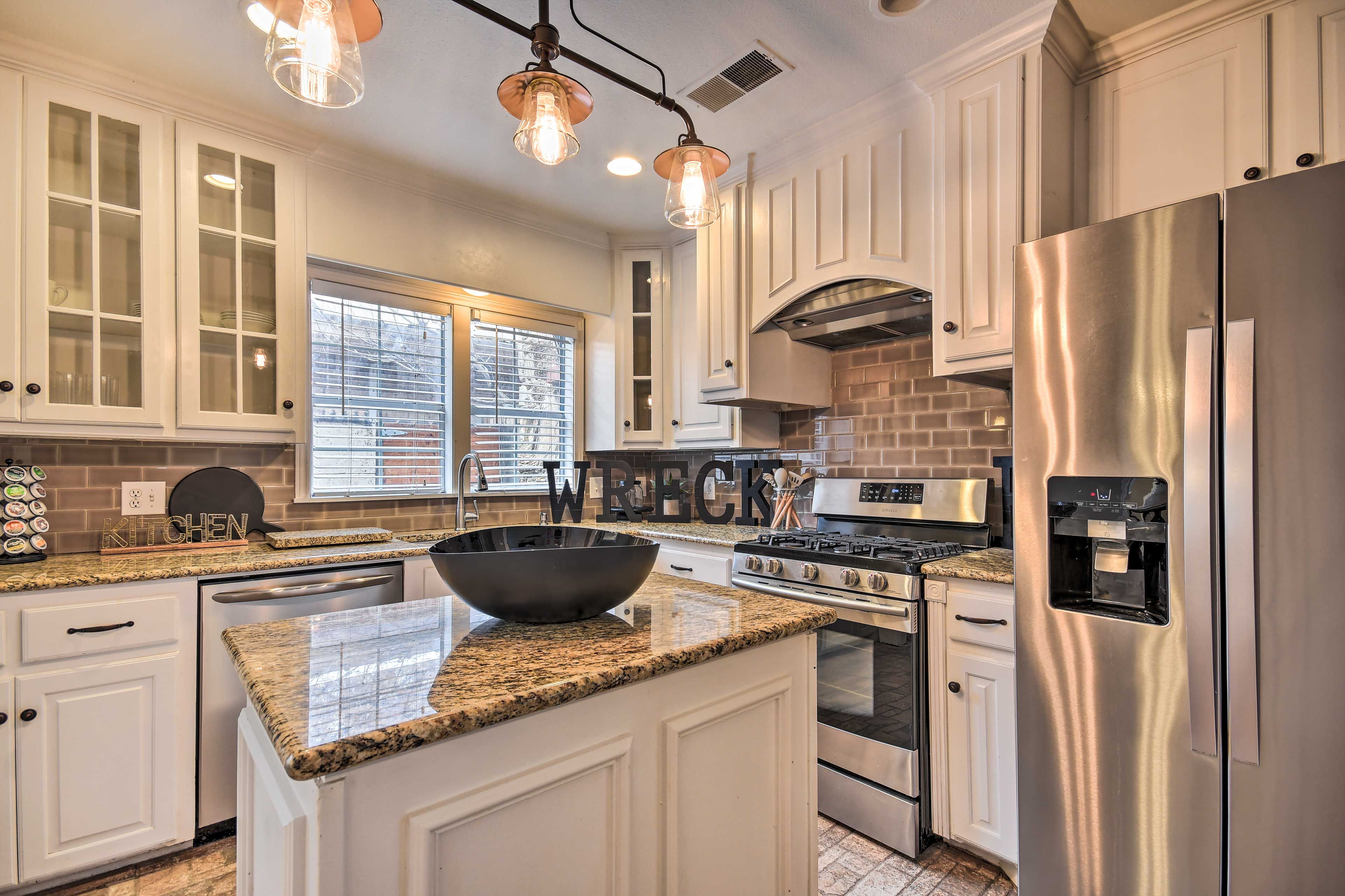 A modern kitchen with white cabinetry, a large island with a black bowl, stainless steel appliances, and pendant lighting.