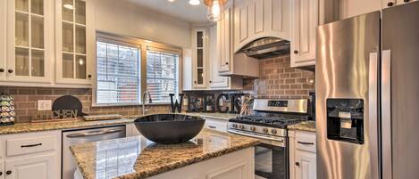 A modern kitchen with white cabinetry, a large island with a black bowl, stainless steel appliances, and pendant lighting.