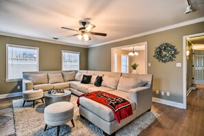 A living room with a sectional sofa, a round coffee table, a small ottoman, a ceiling fan, and a fireplace. - Walk to Texas Tech! Upscale Family Retreat (Lubbock)