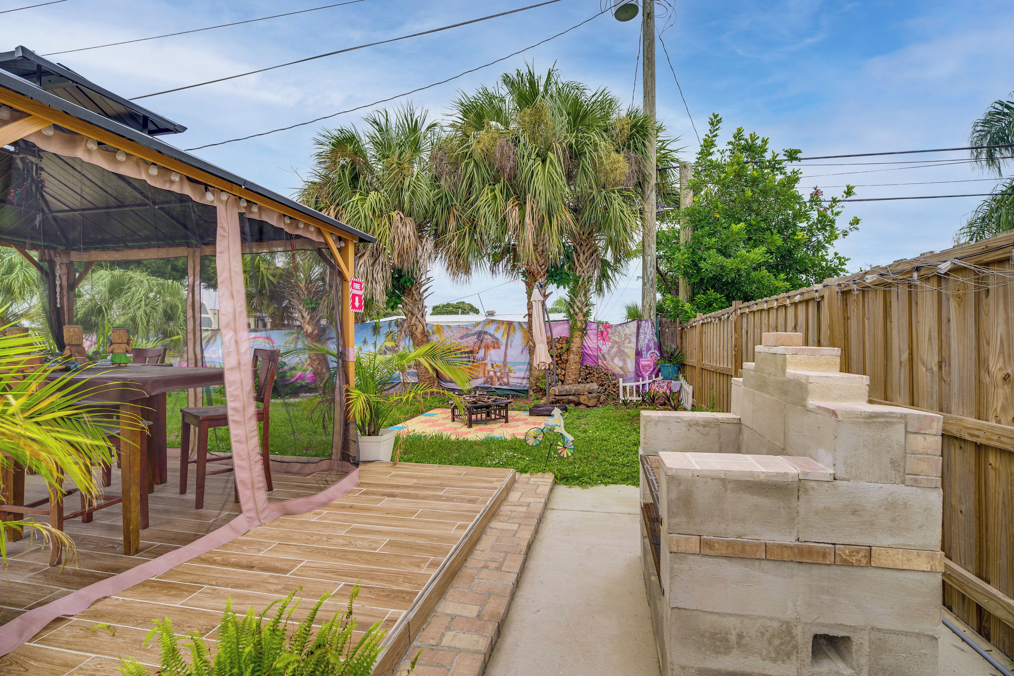 A covered outdoor seating area with a table and chairs, surrounded by a wooden fence and a mural.
