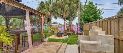 A covered outdoor seating area with a table and chairs, surrounded by a wooden fence and a mural.