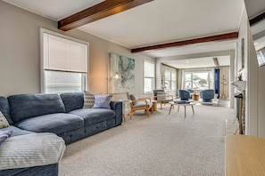 A living room with a blue sofa, wooden chairs, a coffee table, and a large window with blinds.