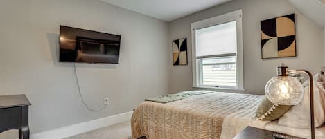 Un dormitorio con una cama, televisión montada en la pared, una ventana y una lámpara.