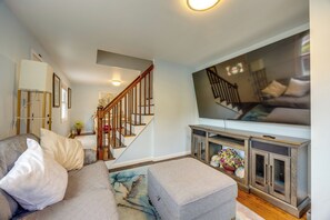 A living room with a sofa, ottoman, and a television on a stand. - Extended Stay Near Yale: East Haven Home w/ Yard! (New Haven)