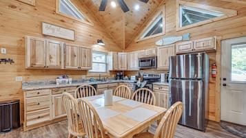 A wooden cabin interior with a kitchen, dining area, and a ceiling fan.