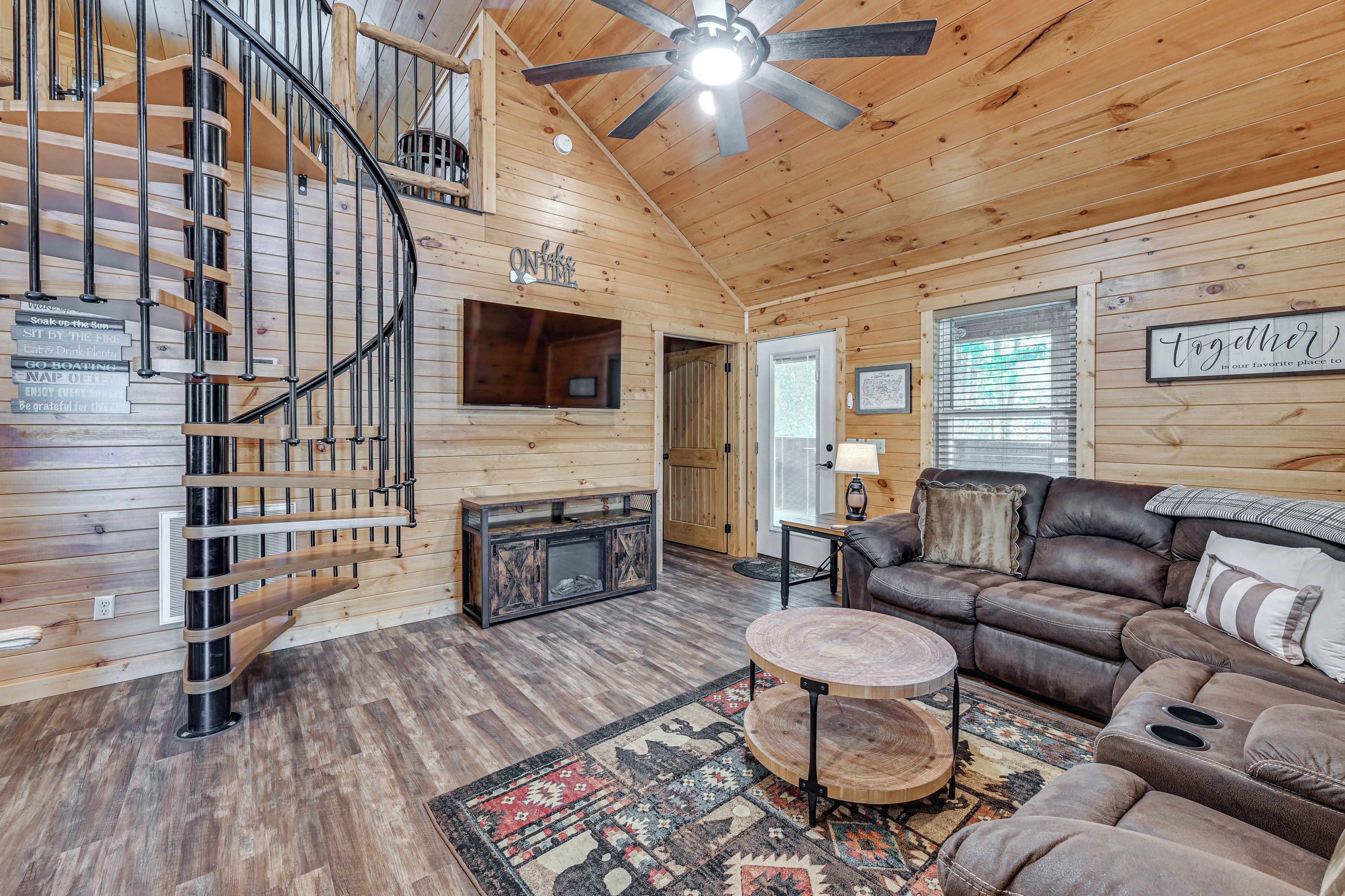 A wooden interior with a spiral staircase, a fireplace, a sofa, and a ceiling fan.