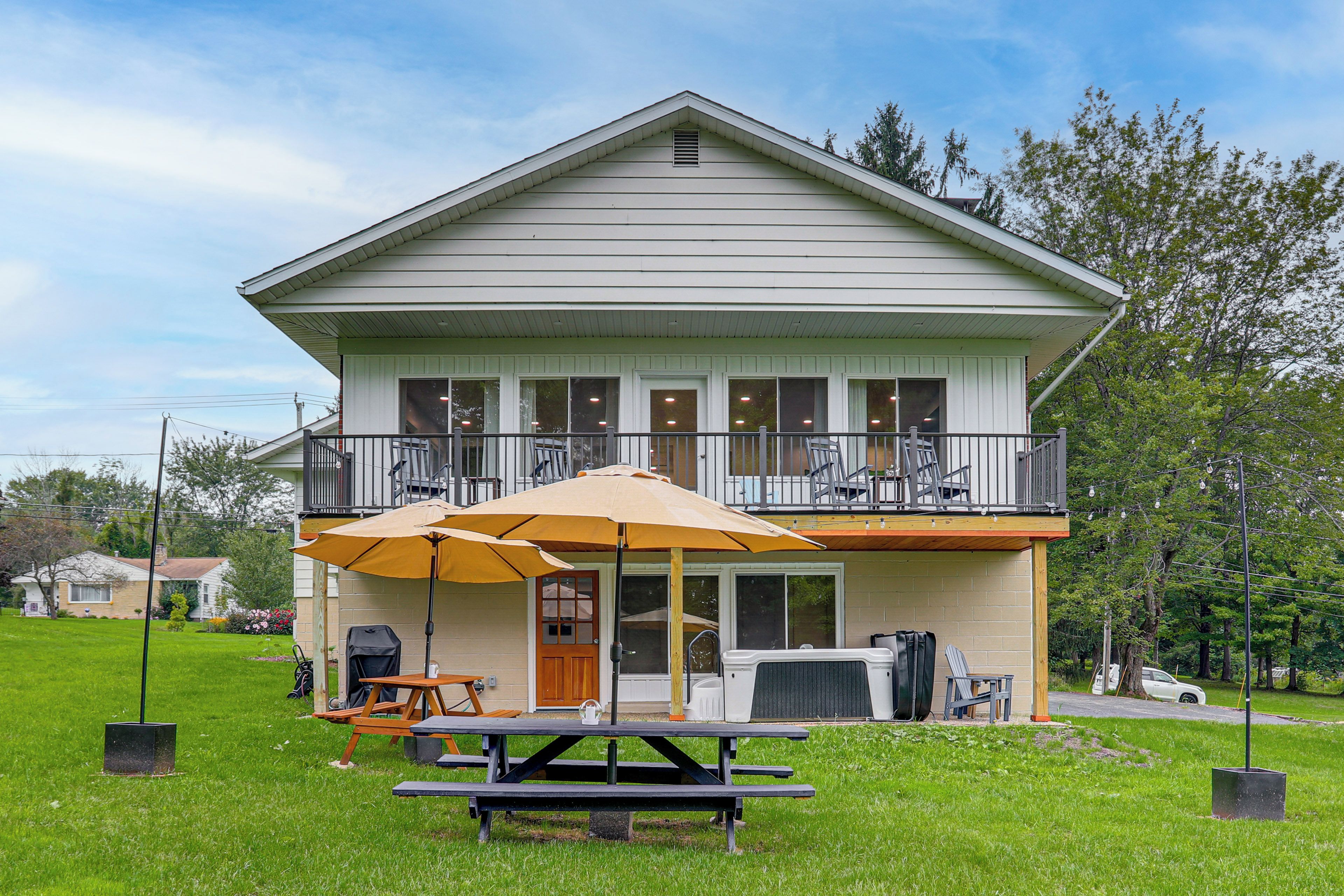 A two-story house with a balcony, a covered patio area with tables and chairs, and a lawn in front.
