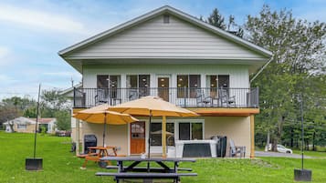 A two-story house with a balcony, a covered patio area with tables and chairs, and a lawn in front.