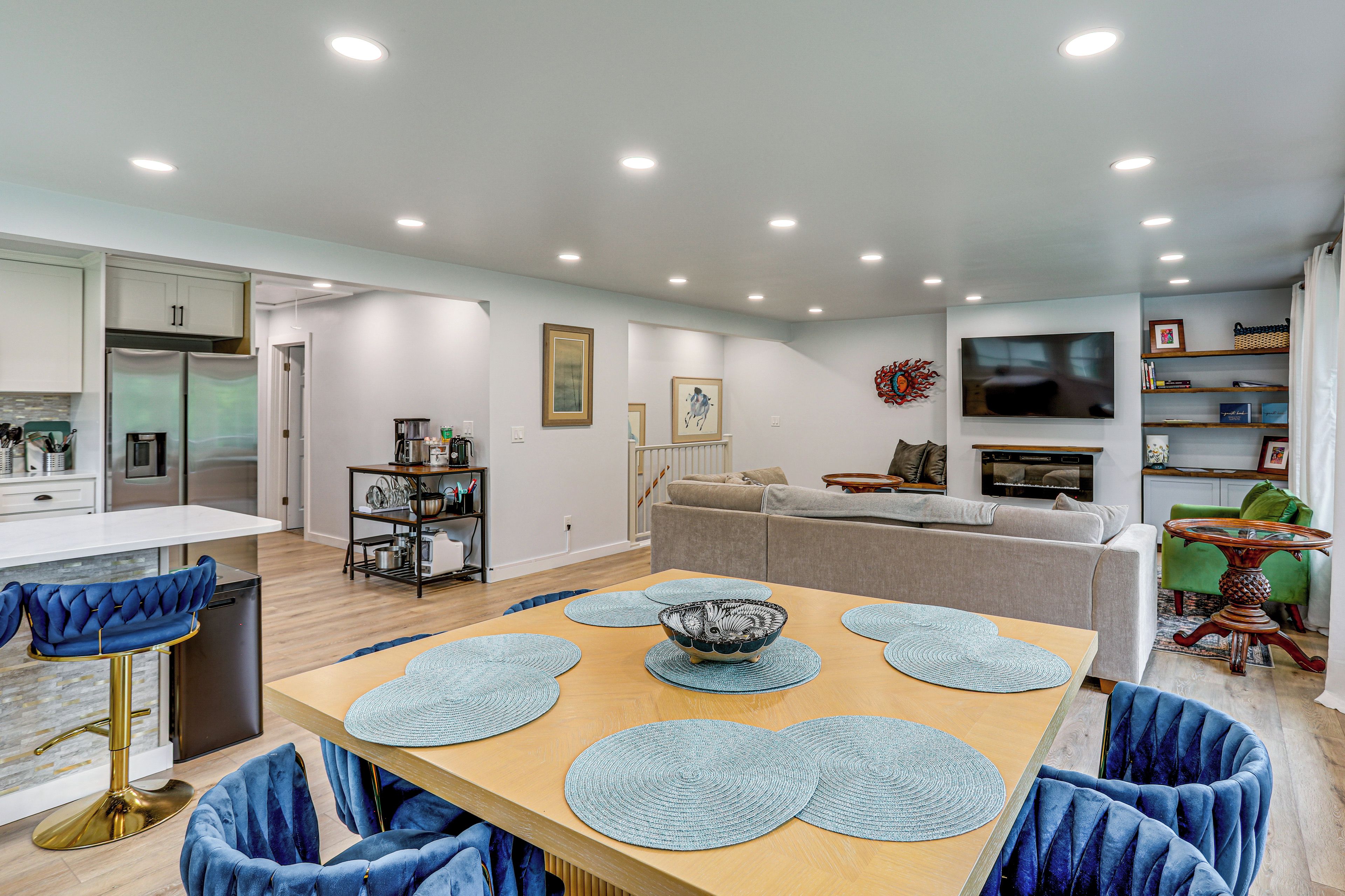 A modern living room with a dining area, a kitchen, and a TV mounted on the wall.