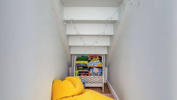 A narrow room with a sloped ceiling, a bed with a yellow blanket, and a bookshelf filled with books.