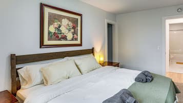 A bedroom with a wooden bed, white bedding, a framed floral artwork, a bedside lamp, and a green towel.