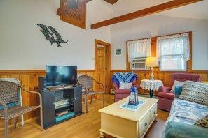 Ein Wohnzimmer mit Fernseher, Korbsesseln, einem roten Sofa und einem kleinen Tisch mit einer Lampe.