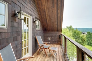Eine Holzterrasse mit zwei Stühlen und einem kleinen Tisch, mit Blick auf eine grüne Landschaft.
