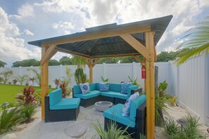 A covered outdoor seating area with a wooden pergola, a curved blue sofa, and a round table.
