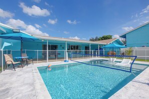A swimming pool with a blue fence, lounge chairs, and umbrellas.