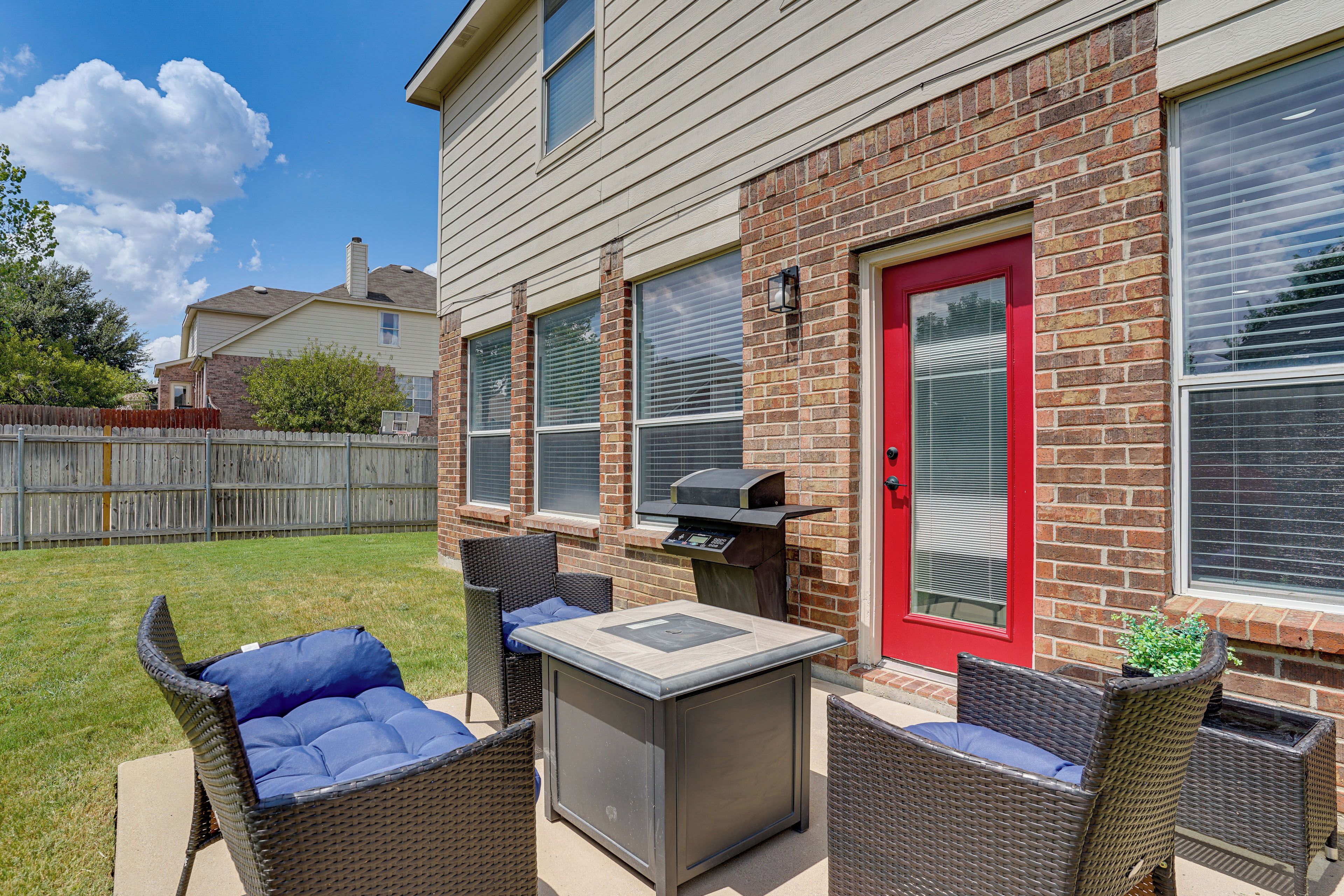 Une terrasse extérieure avec un barbecue, des meubles en osier et une porte rouge.