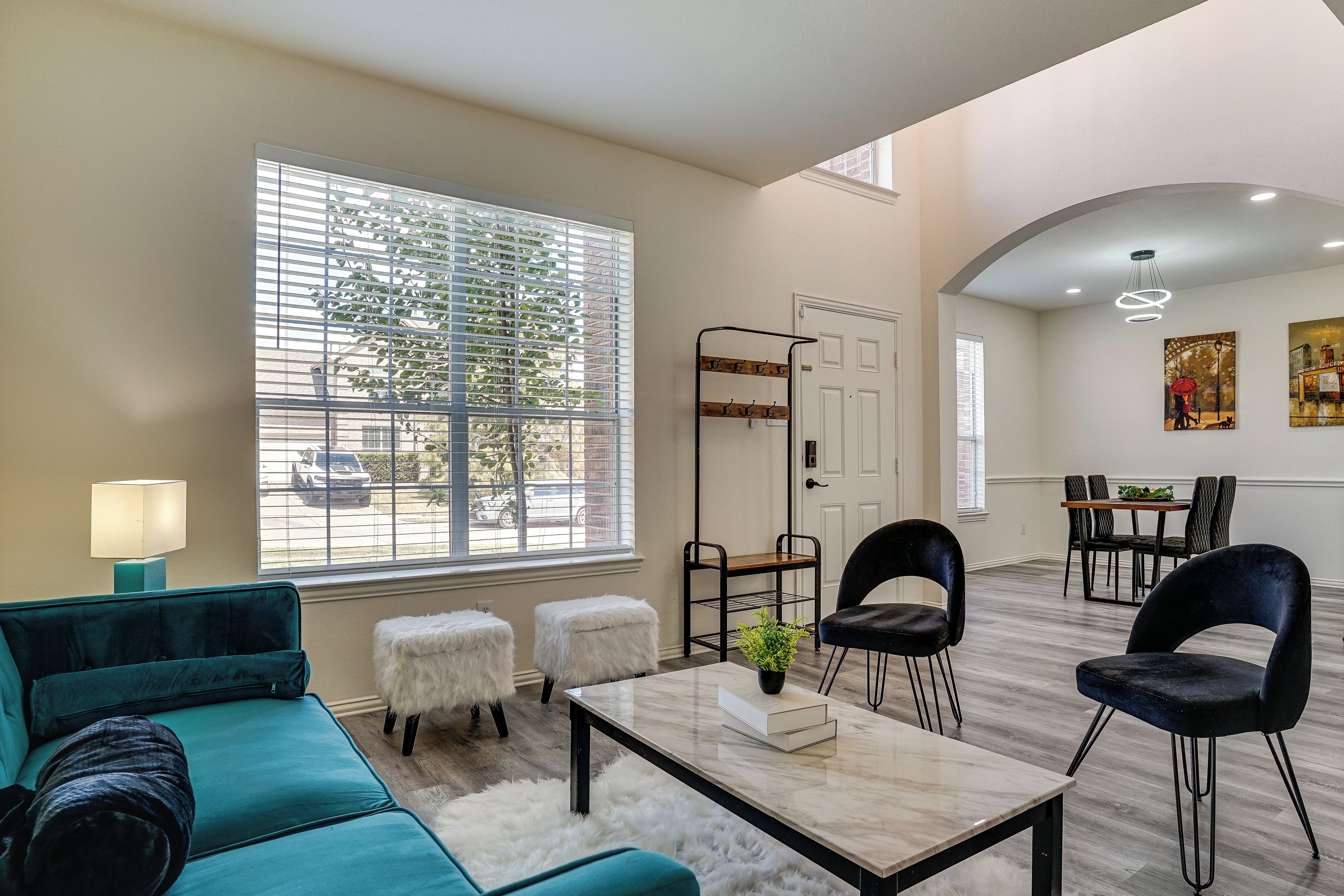 A modern living room with a teal sofa, a coffee table, and a dining area with chairs and a table.