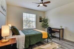 A bedroom with a bed, desk, chair, lamp, window, and ceiling fan.