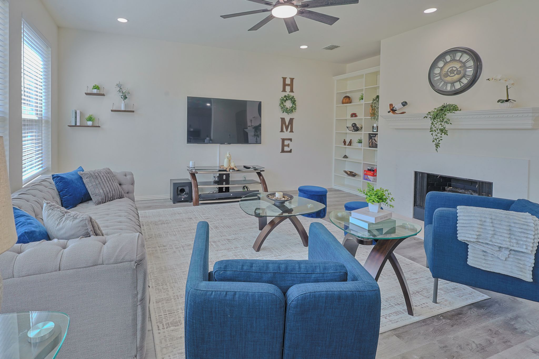 A modern living room with a sofa, two armchairs, a coffee table, a flat-screen TV, and a fireplace.