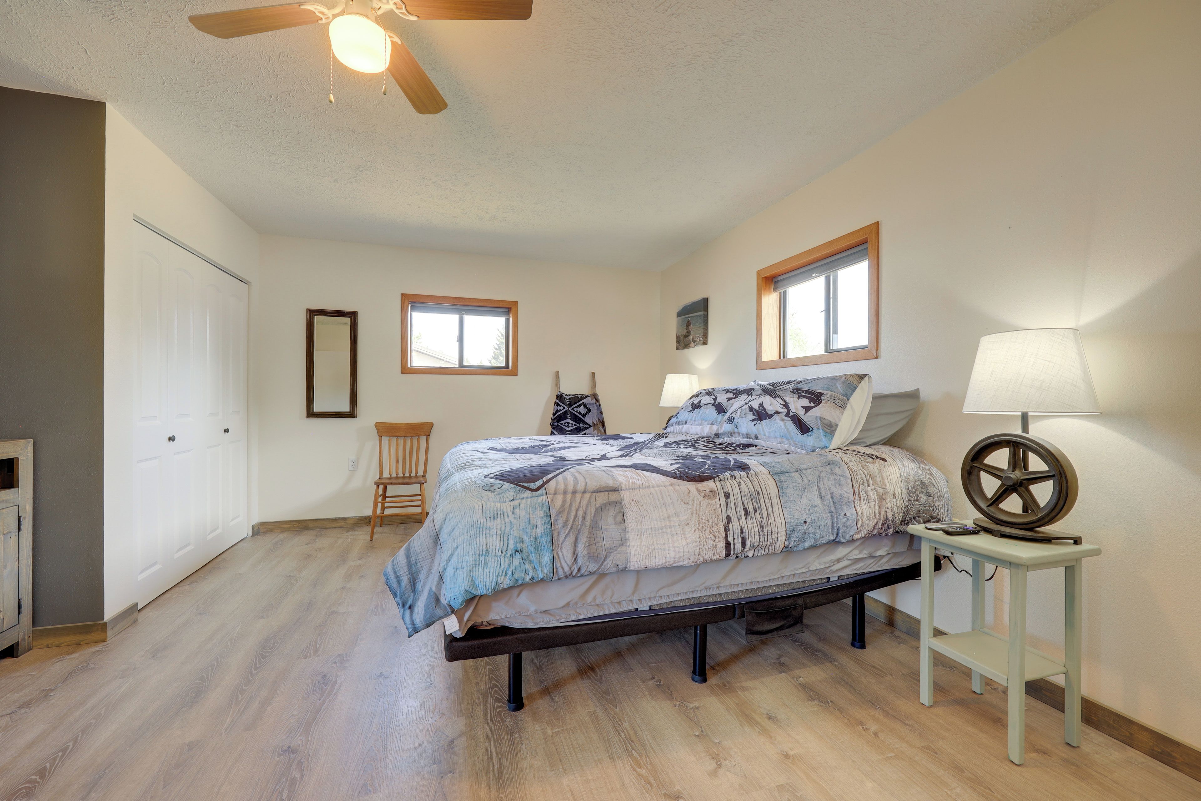 A bedroom with a bed, a chair, a nightstand, a lamp, and a ceiling fan.