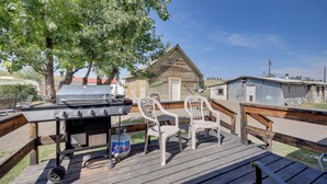 Une terrasse en bois avec un barbecue et des chaises, un petit bâtiment en bois et un ciel bleu dégagé.