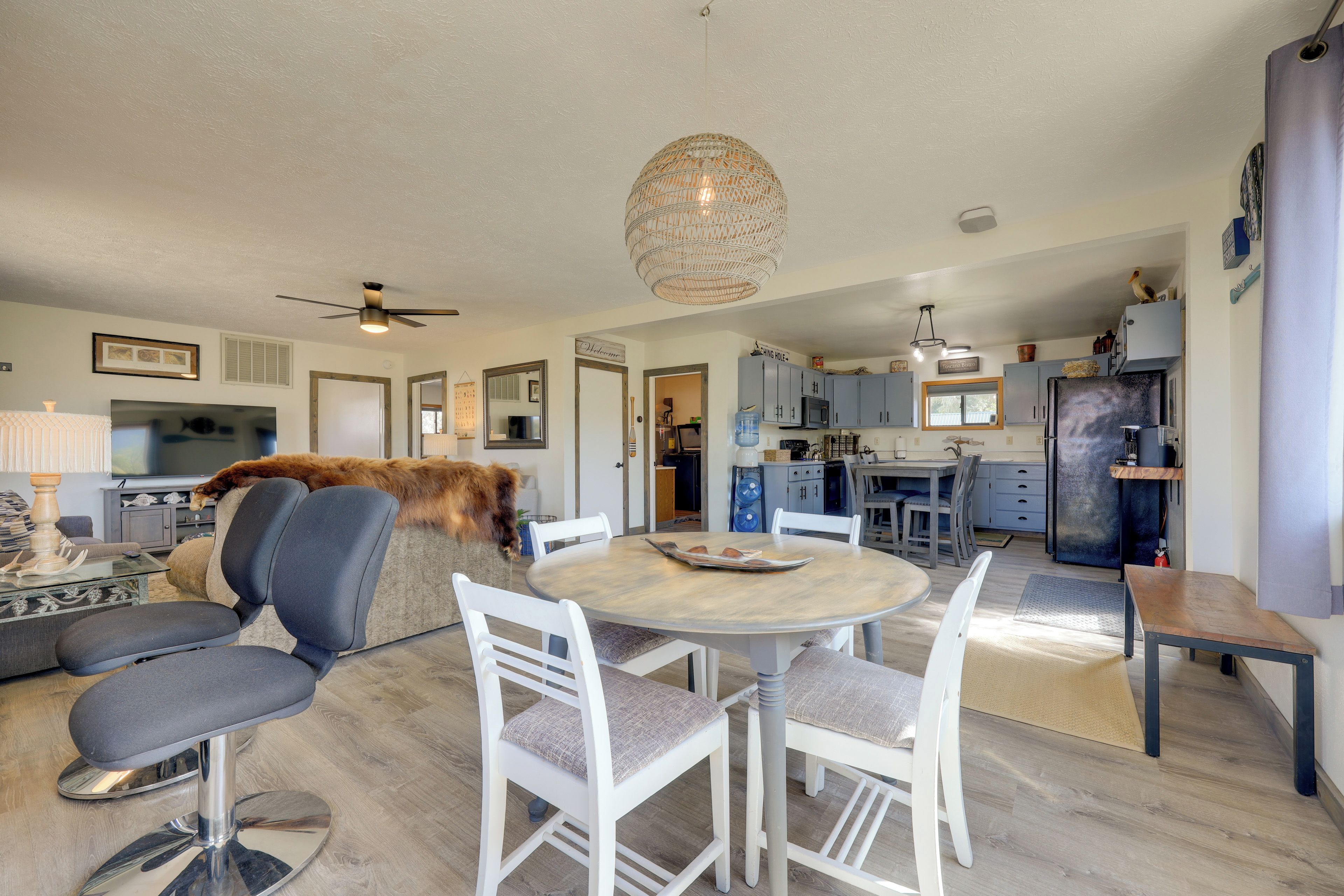 A modern kitchen with a dining area, a living room with a sofa and a television, and a ceiling fan.