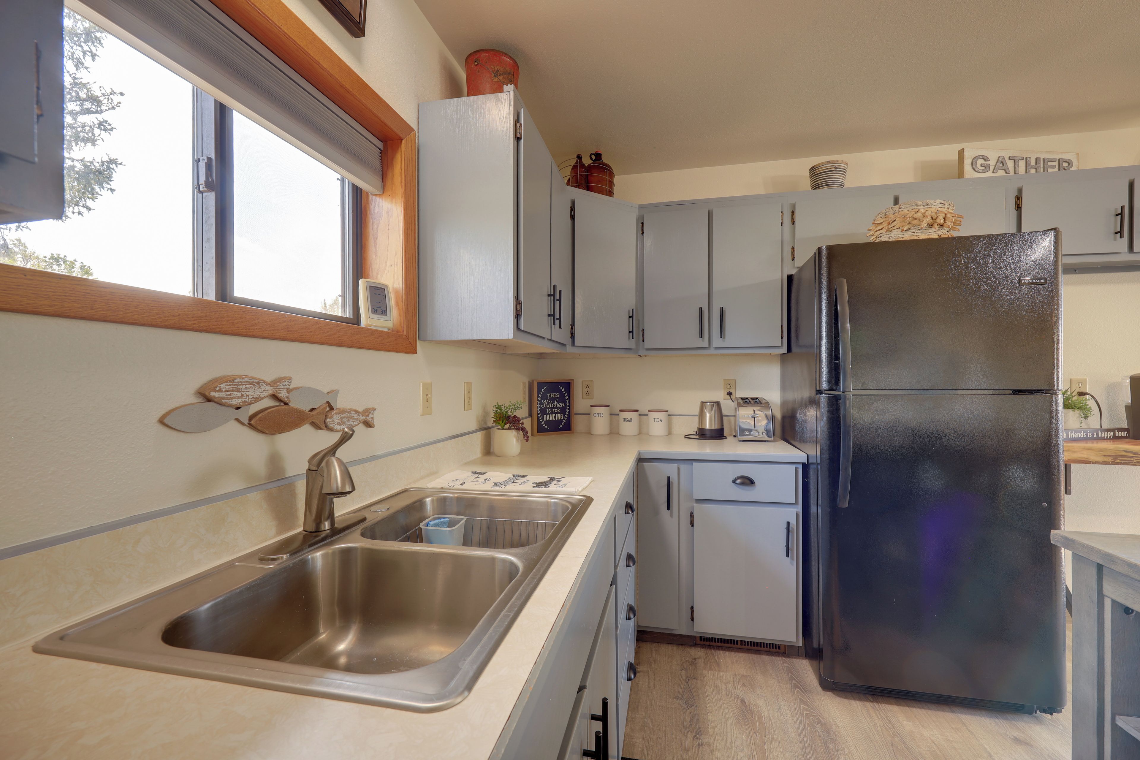 A compact kitchen with a stainless steel sink, a black refrigerator, and light grey cabinets.