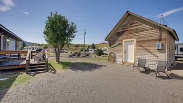 A gravel driveway leading to a wooden cabin with a door and a window, a metal chair, and a small table with chairs outside.