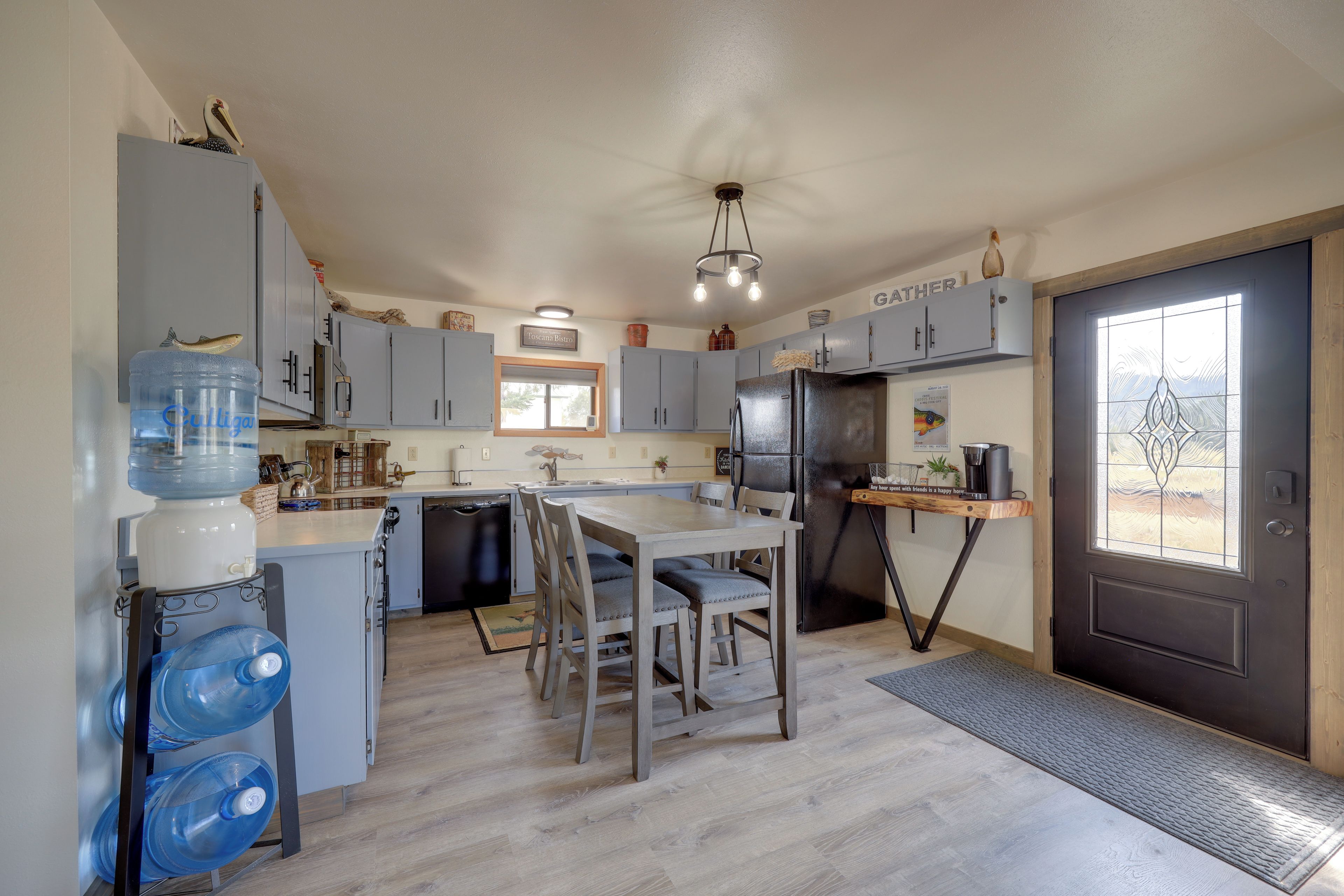 Una cocina con armarios grises, un refrigerador negro, una mesa de comedor de madera y un dispensador de agua.